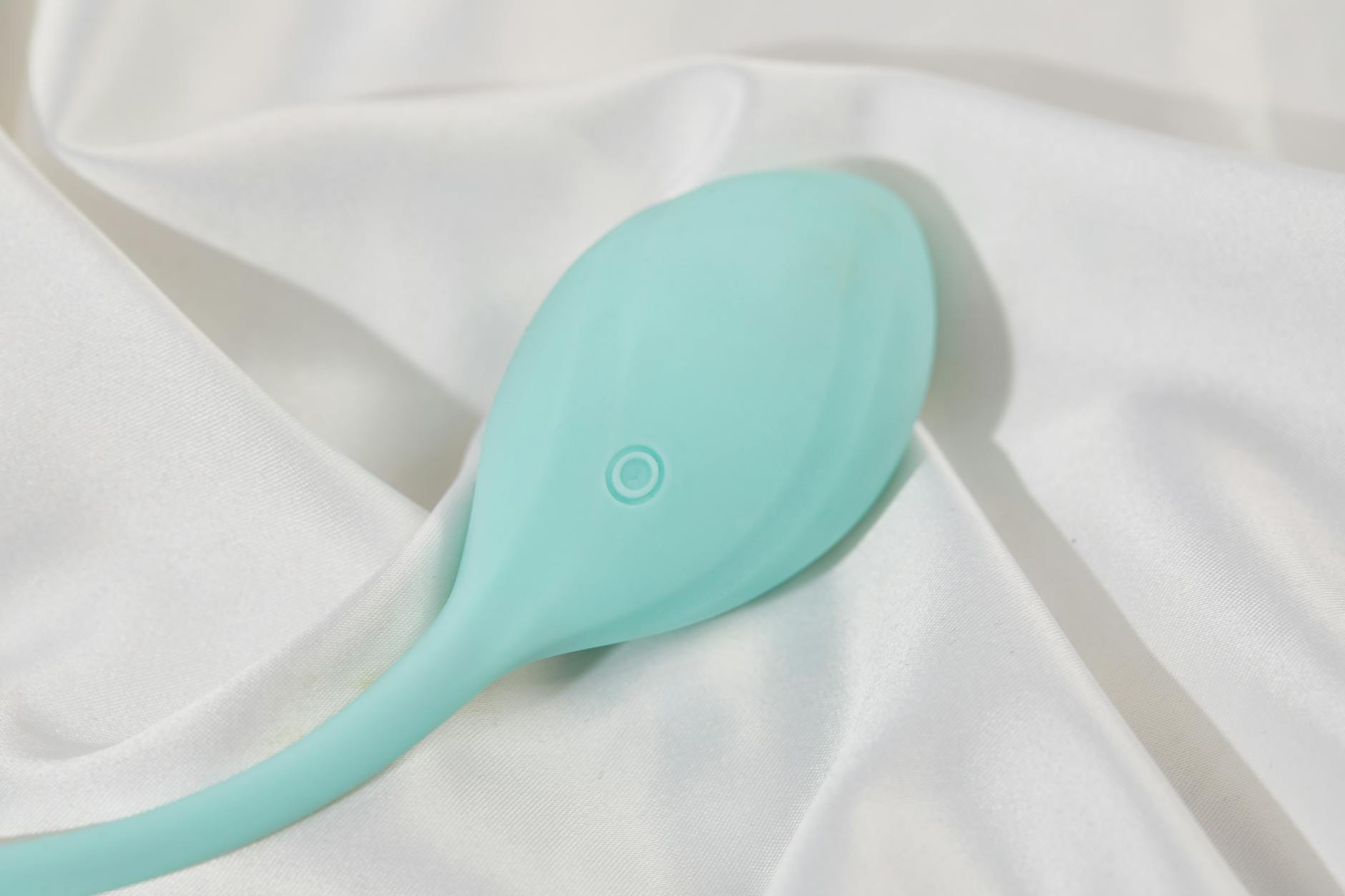 A sleek teal clitoral vibrator on smooth white silk, symbolizing accessible and comfortable solo pleasure.