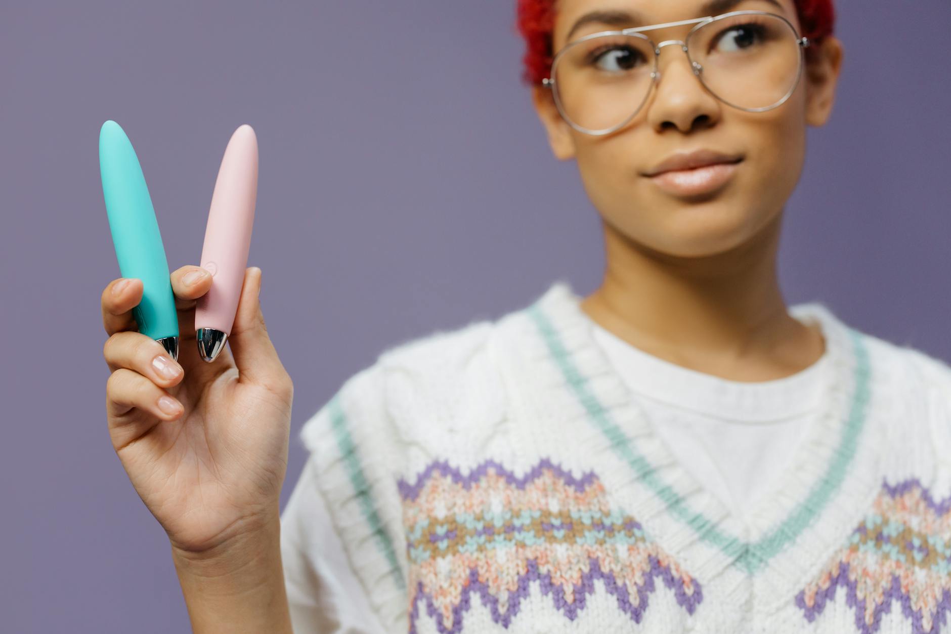 A person holding two colorful vibrators against a purple background