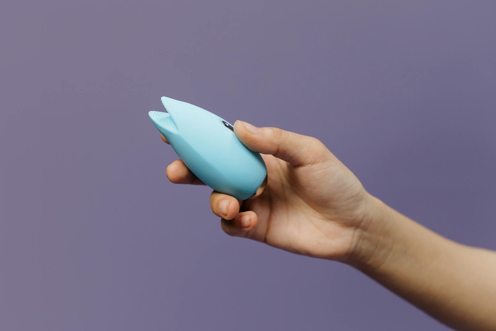 A blue silicone clitoral vibrator held in hand, representing modern pleasure tools for sexual wellness.