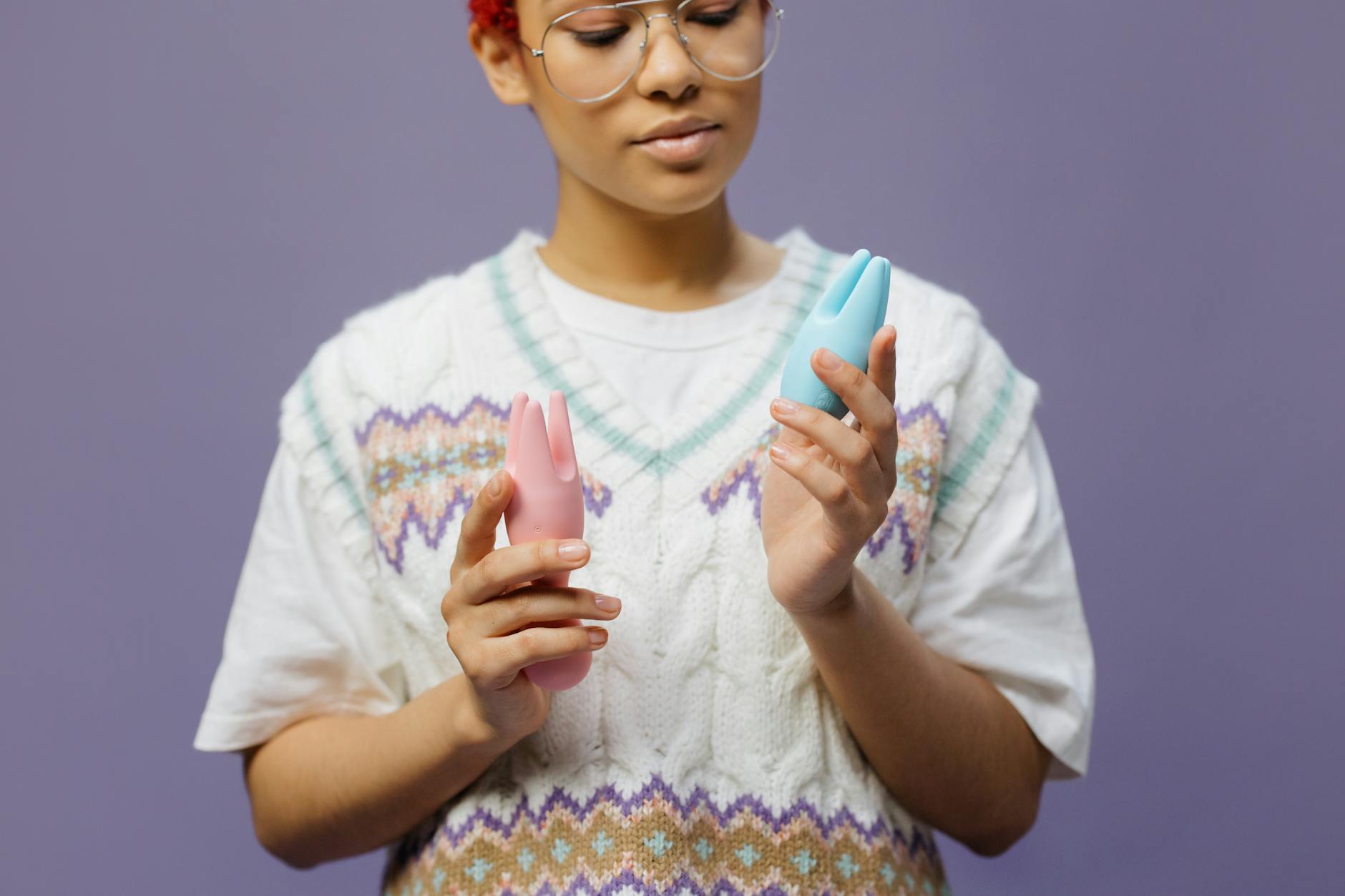 Hand holding a blue silicone clitoral vibrator against a purple background, symbolizing mindful pleasure and self-care.