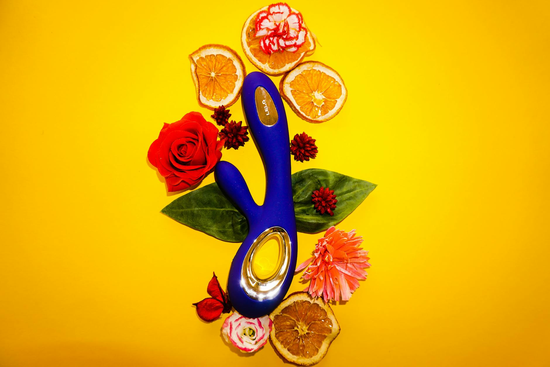 Foto eines farbigen Vibrators auf gelbem Hintergrund mit Blüten, die kunstvoll angeordnet sind